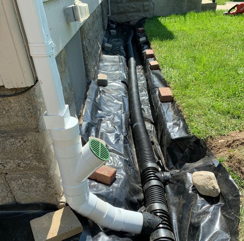 Perimeter drain tile installation beside house foundation with waterproofing membrane and drainage pipe
